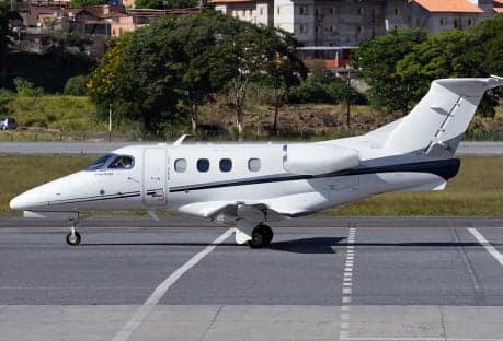 A Phenom 100 aircraft parked in a hangar with a white, black, and red paint scheme.