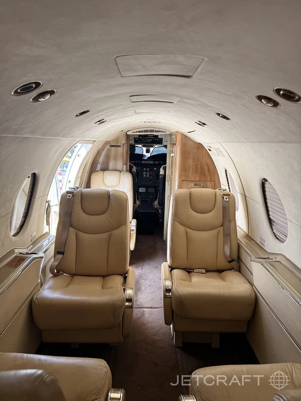 The interior cabin of a private jet with tan leather seats and a view into the cockpit.