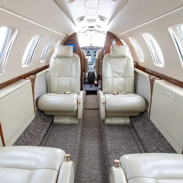 A view inside an aircraft cabin with light beige leather seats, looking towards the cockpit with a fire extinguisher visible.
