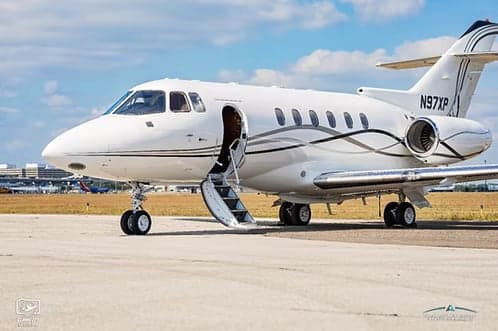 A white jet aircraft with registration N97XP parked on the tarmac with the airstair door open.