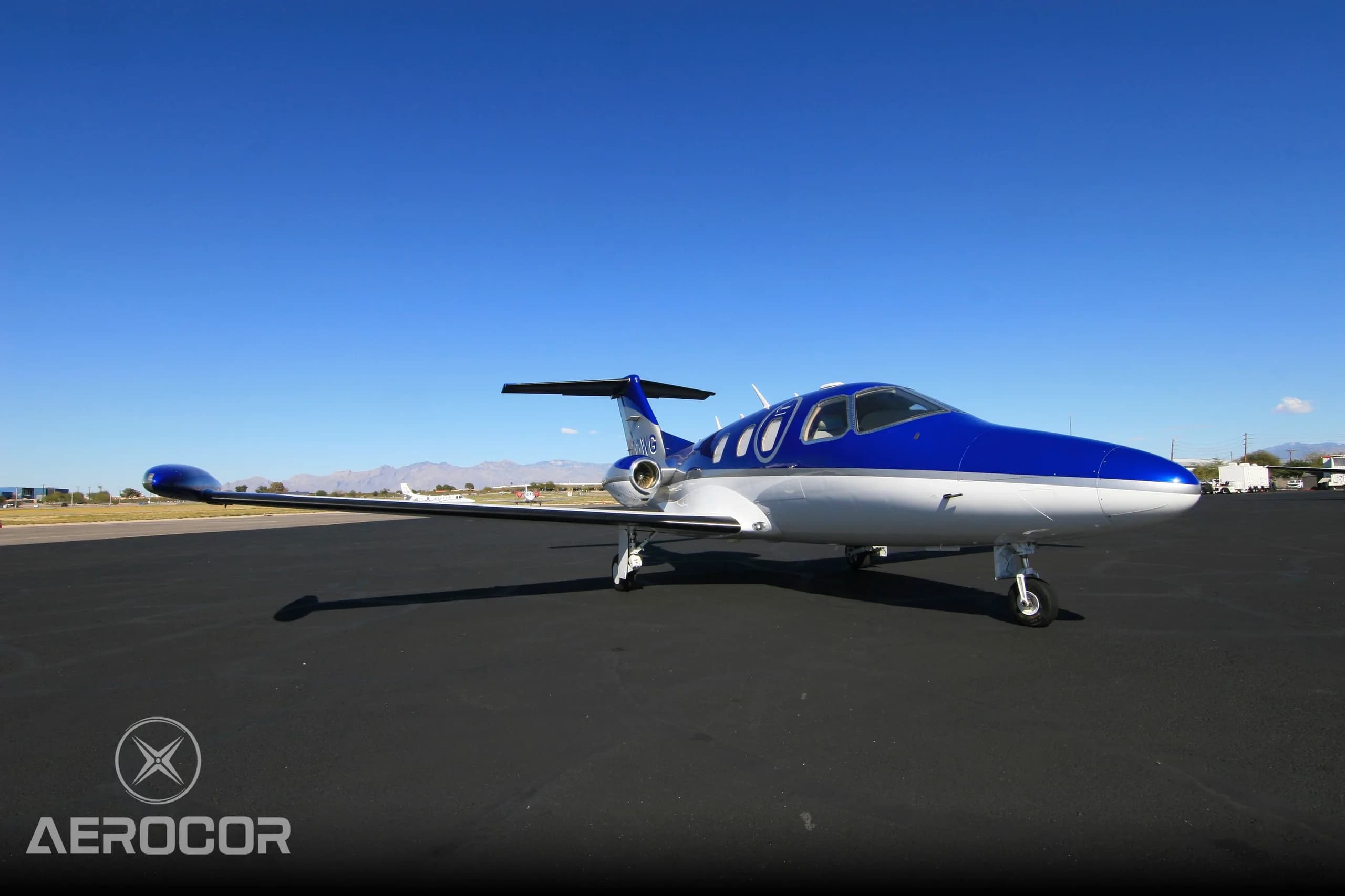 A front-side view of the blue and white Eclipse 500/550 jet, N712WG, parked on an airport tarmac.