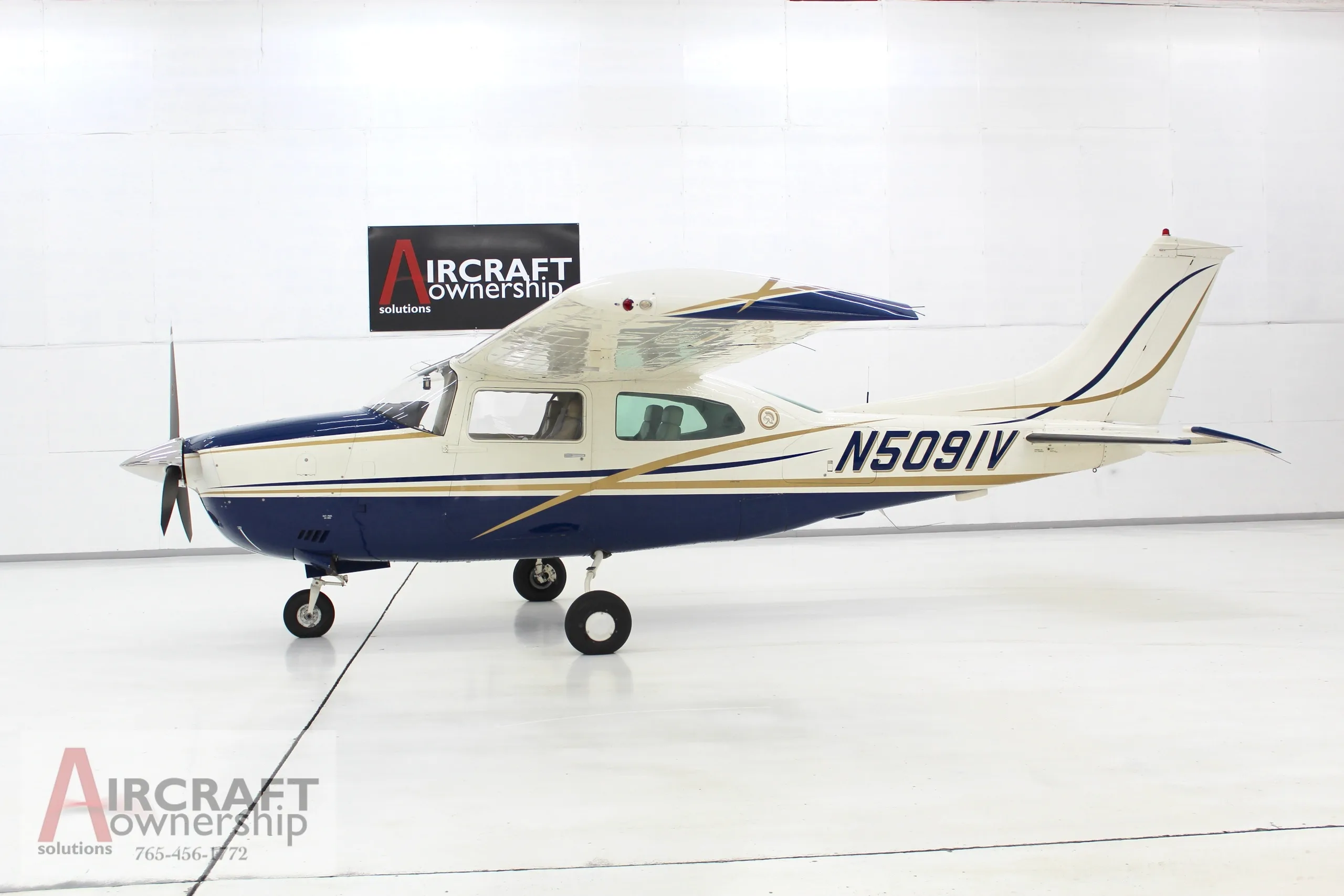 A blue and white Cessna 206 aircraft, N5091V, parked in a brightly lit hangar.