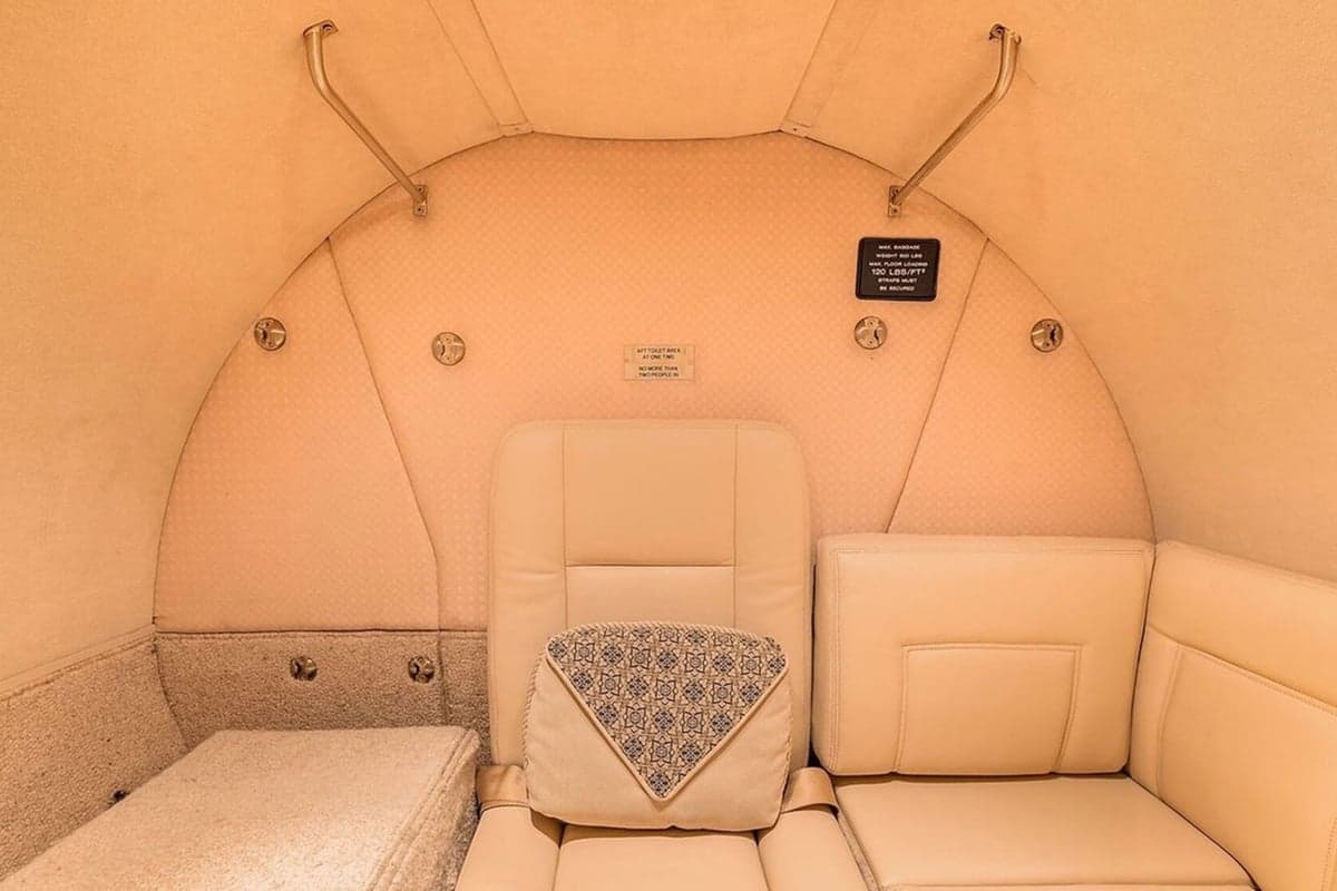 A cozy section of a private jet's cabin interior with a beige bench seat and a single seat.