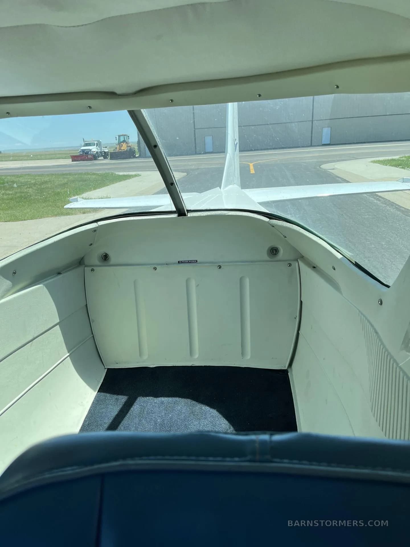 The empty rear cabin area of a small aircraft, viewed from the front seats, with a view of the tarmac and a tractor outside.