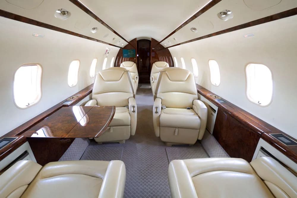 View of the aircraft cabin showing a cream-colored leather seat and wood table.