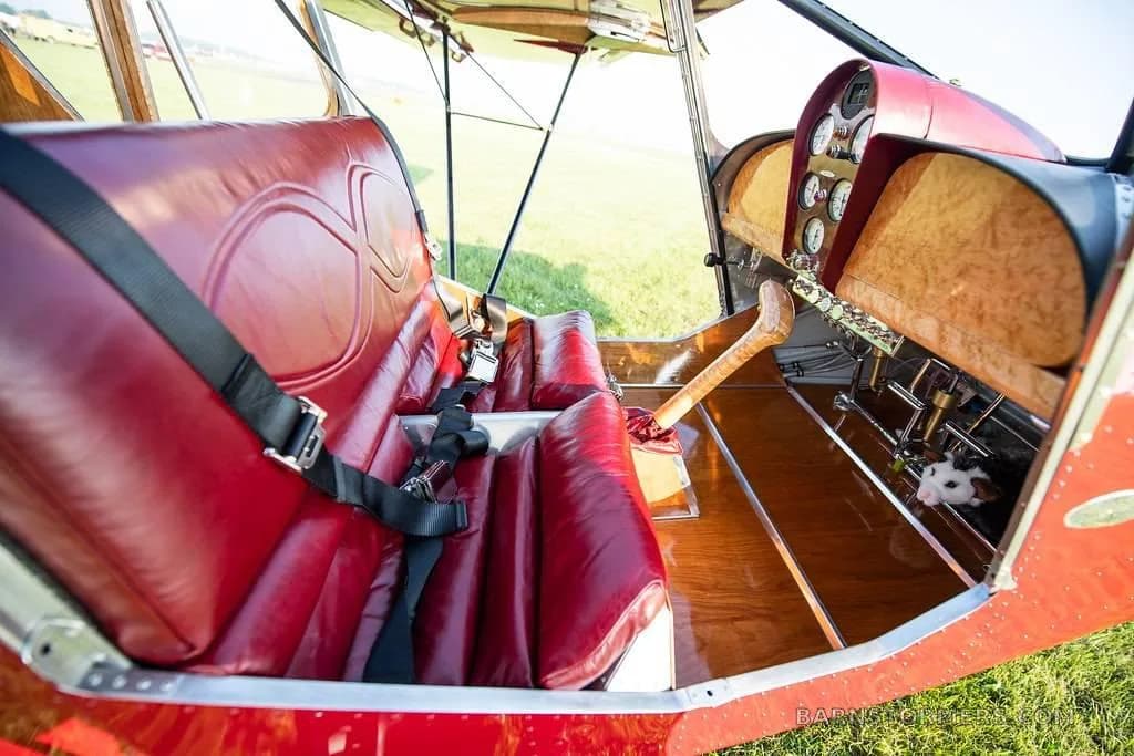 The red leather seats and wooden floor of an aircraft cabin, with a partial view of the instrument panel and a small toy peeking out.