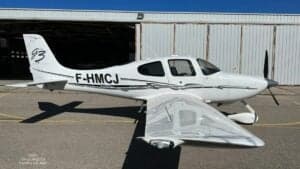 A Cirrus SR22 G3 aircraft with registration F-HMCJ parked on the tarmac in front of a hangar.