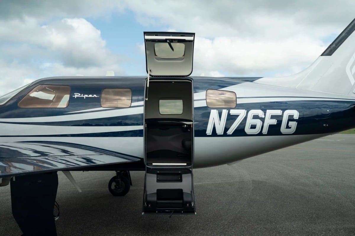 The Piper M700 Fury aircraft with its main cabin door open, revealing the interior steps and the N-number N76FG on the fuselage.