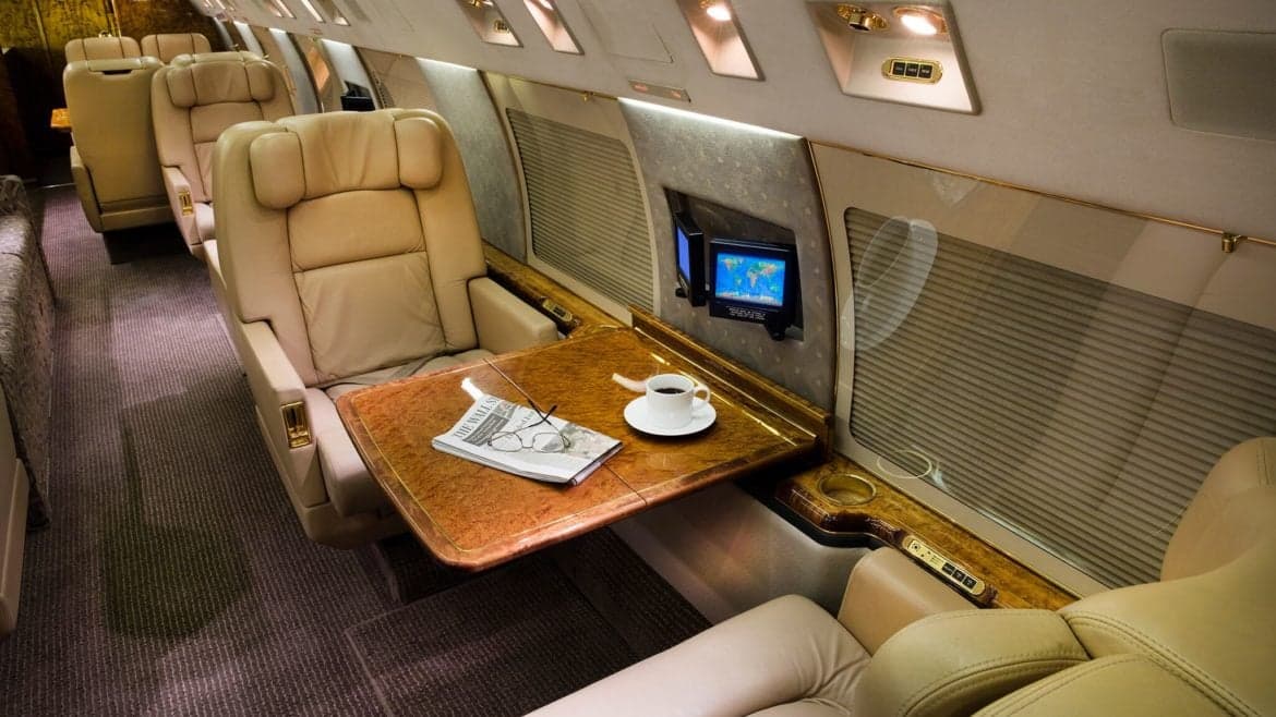 Close-up of a leather seat with a wooden table, newspaper, and coffee cup inside the aircraft.