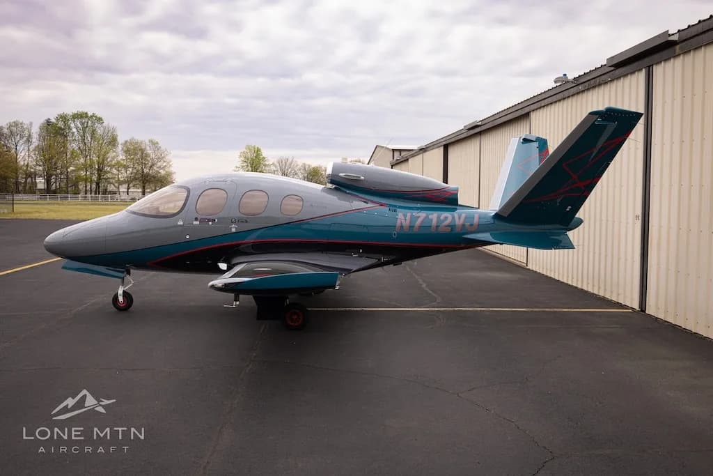 A three-quarter rear view of the Cirrus Vision Jet (N712VJ) in grey and teal, parked on an airfield.
