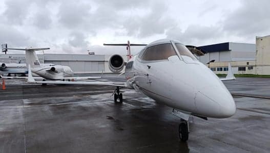 A Learjet aircraft is parked on the tarmac in front of a hangar on a cloudy day.