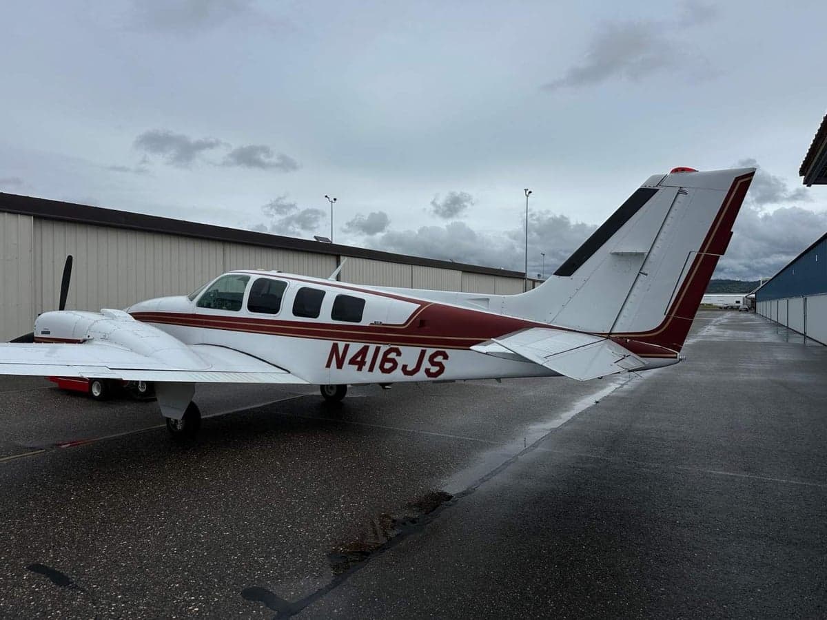 A Beechcraft Baron aircraft with a white and maroon paint scheme is parked on the tarmac.