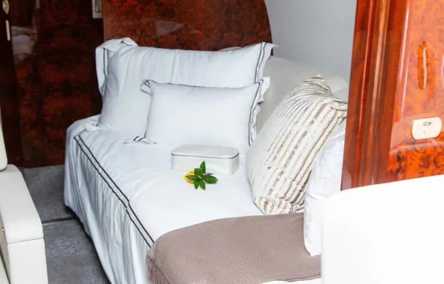A comfortable bed or divan in a private jet cabin, adorned with white bedding and a decorative pillow.