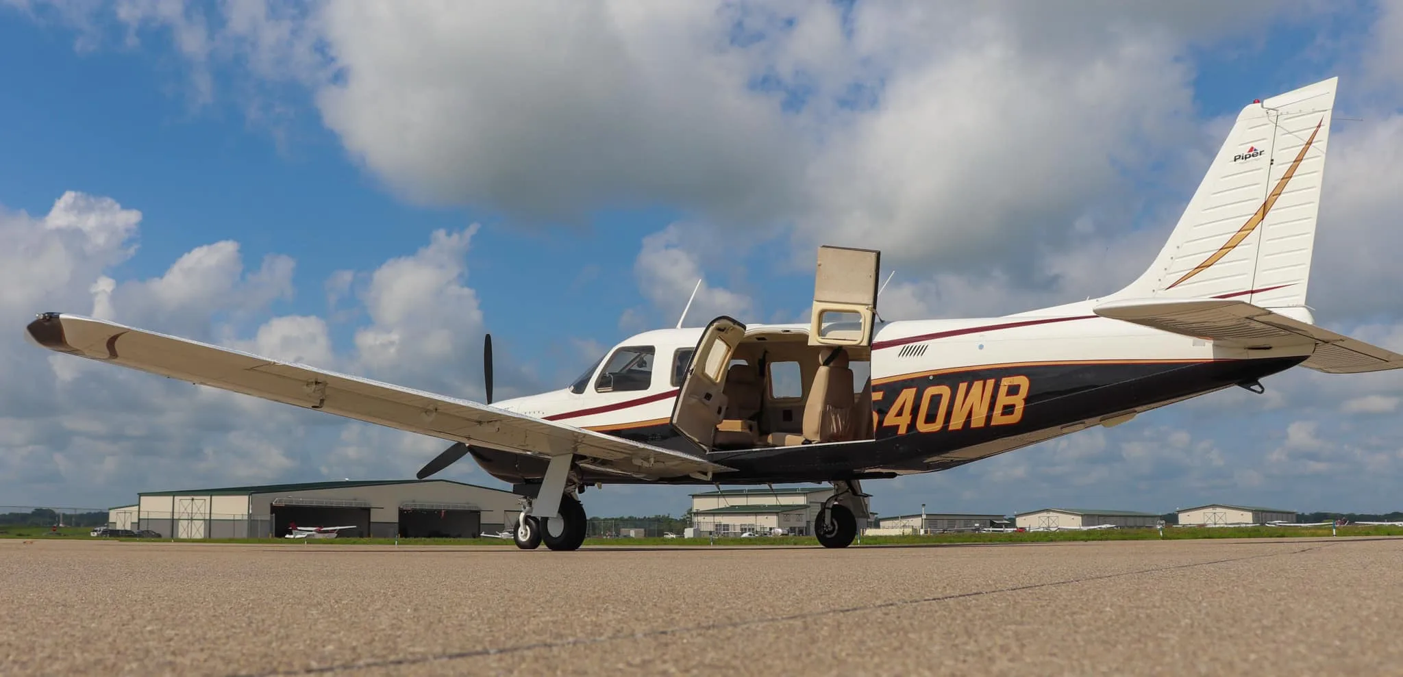 A Piper Saratoga II TC aircraft, N540WB, with its doors open, parked on an airfield under a partly cloudy sky.