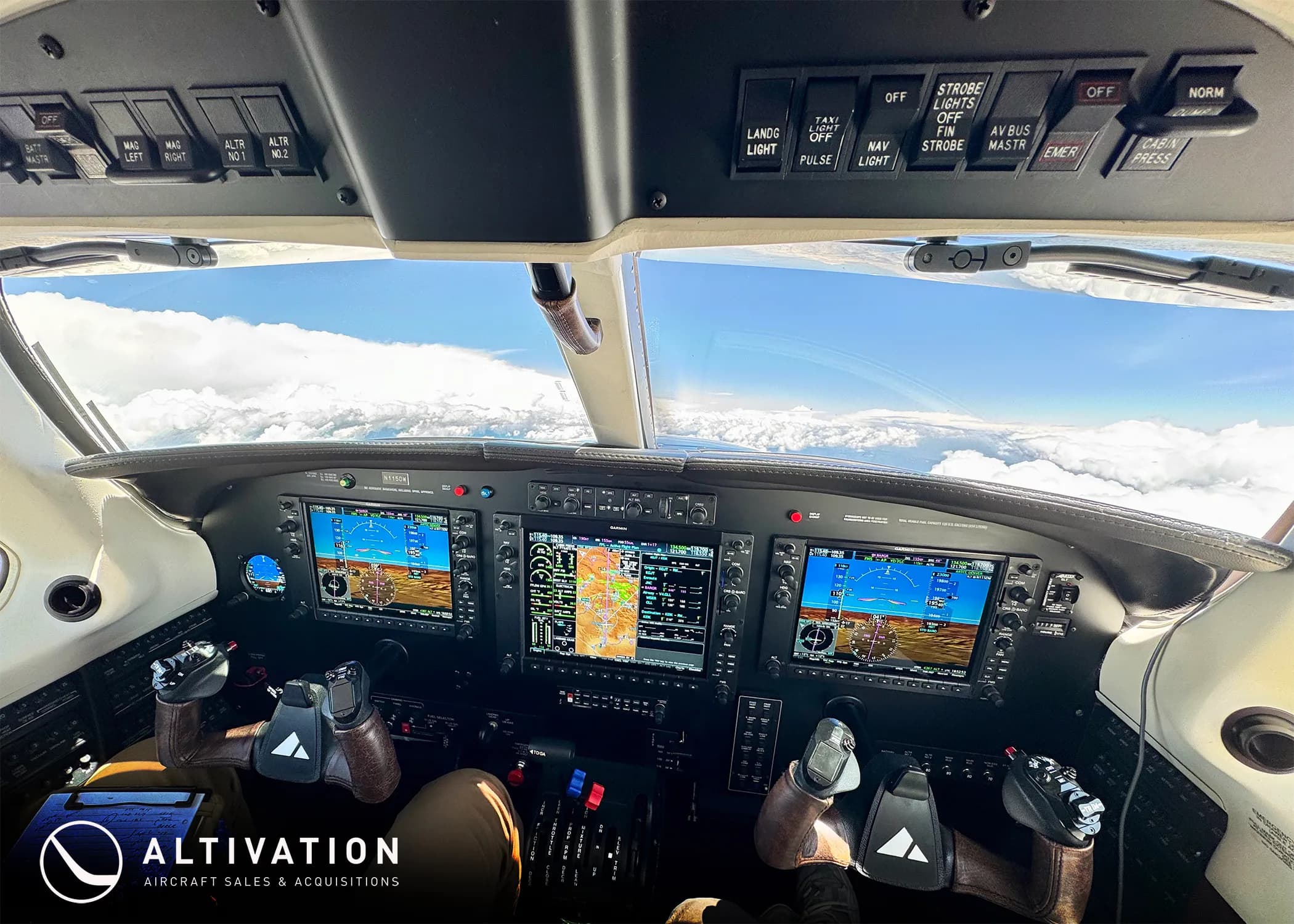 The modern glass cockpit of a Piper M350 aircraft with multiple display screens and controls, flying above clouds.