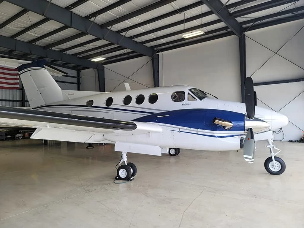 A side view of a white and blue twin-engine turboprop aircraft parked inside a hangar.