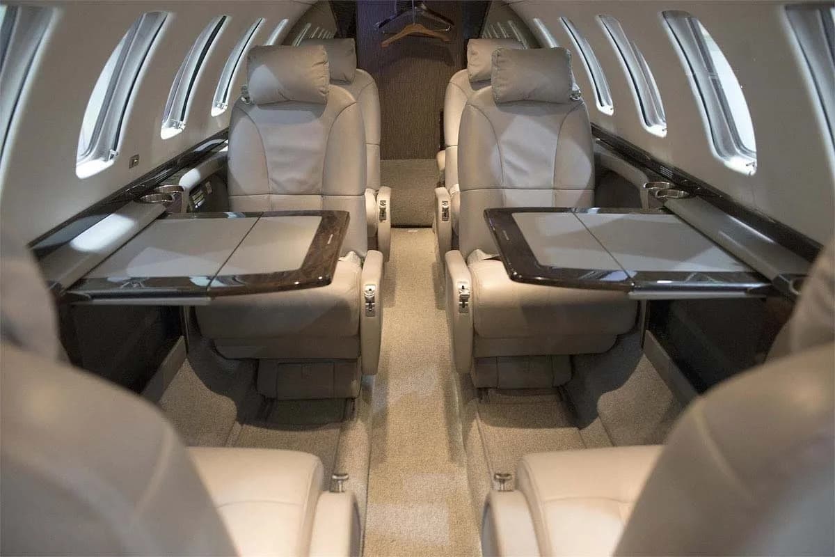 The luxurious interior cabin of a private jet with light-colored leather seats and fold-out tables.