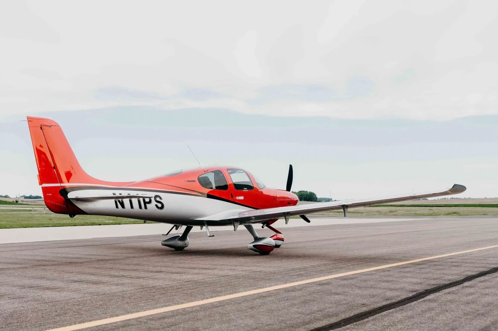 A red and silver Cirrus SR20 Premium aircraft (N11PS) parked on an airfield tarmac.
