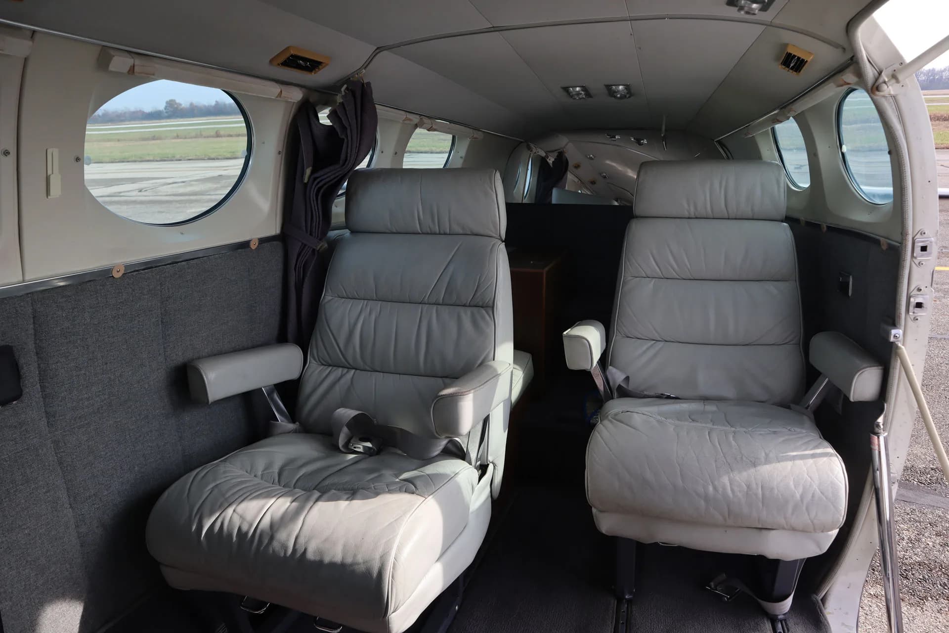 The interior of the aircraft features two gray leather seats with windows in the background.