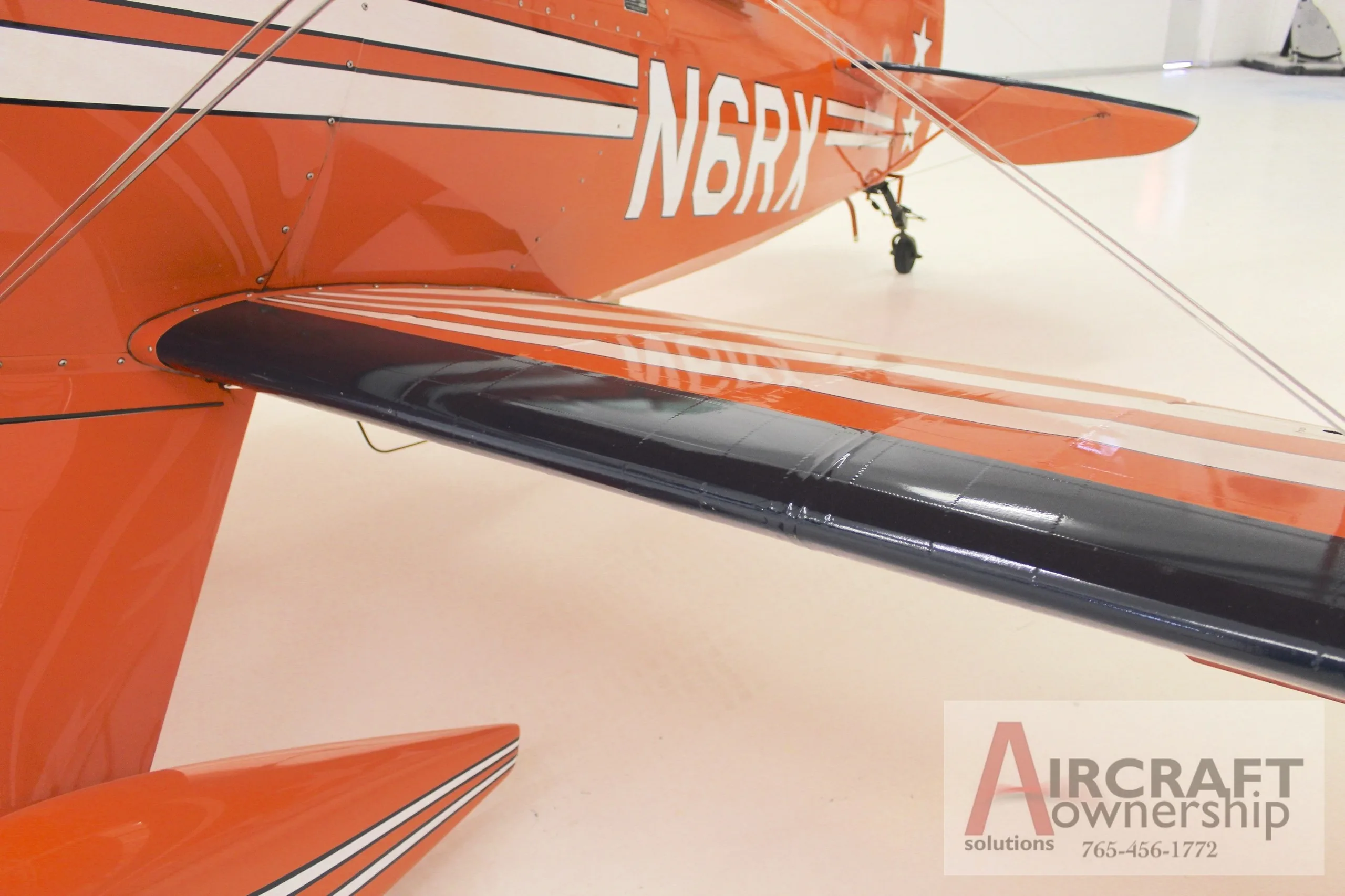 A close-up view of the lower wing and fuselage of an orange Pitts S-1T biplane, showing the N-number.