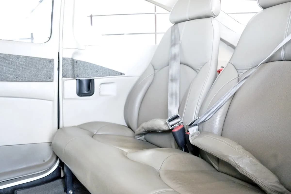 The light grey leather interior cabin seats of a Cessna Skylane, with seatbelts fastened.