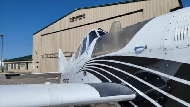 Front-left view of a white agricultural aircraft with black stripes parked in front of a "HUTCHINSON" hangar.