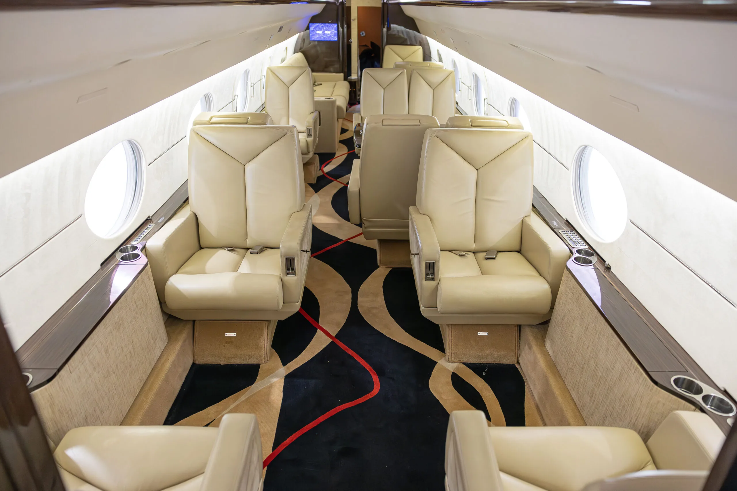 Aircraft interior with cream-colored leather seats and patterned carpet.