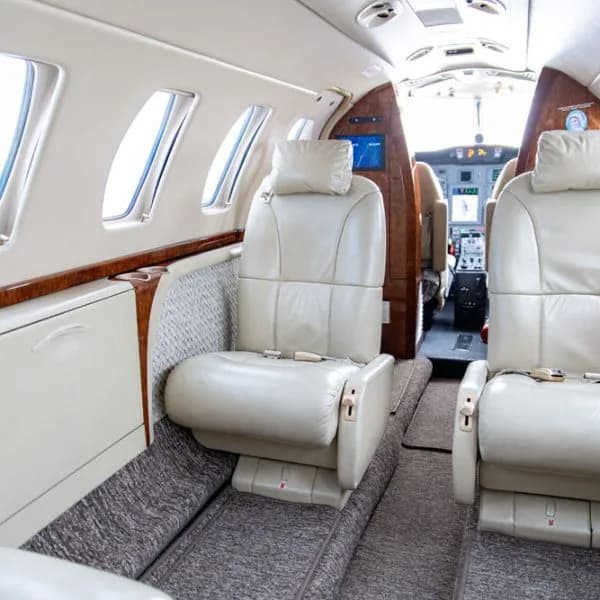 An angled view of an aircraft cabin interior, highlighting a light beige leather seat and the cockpit in the background.
