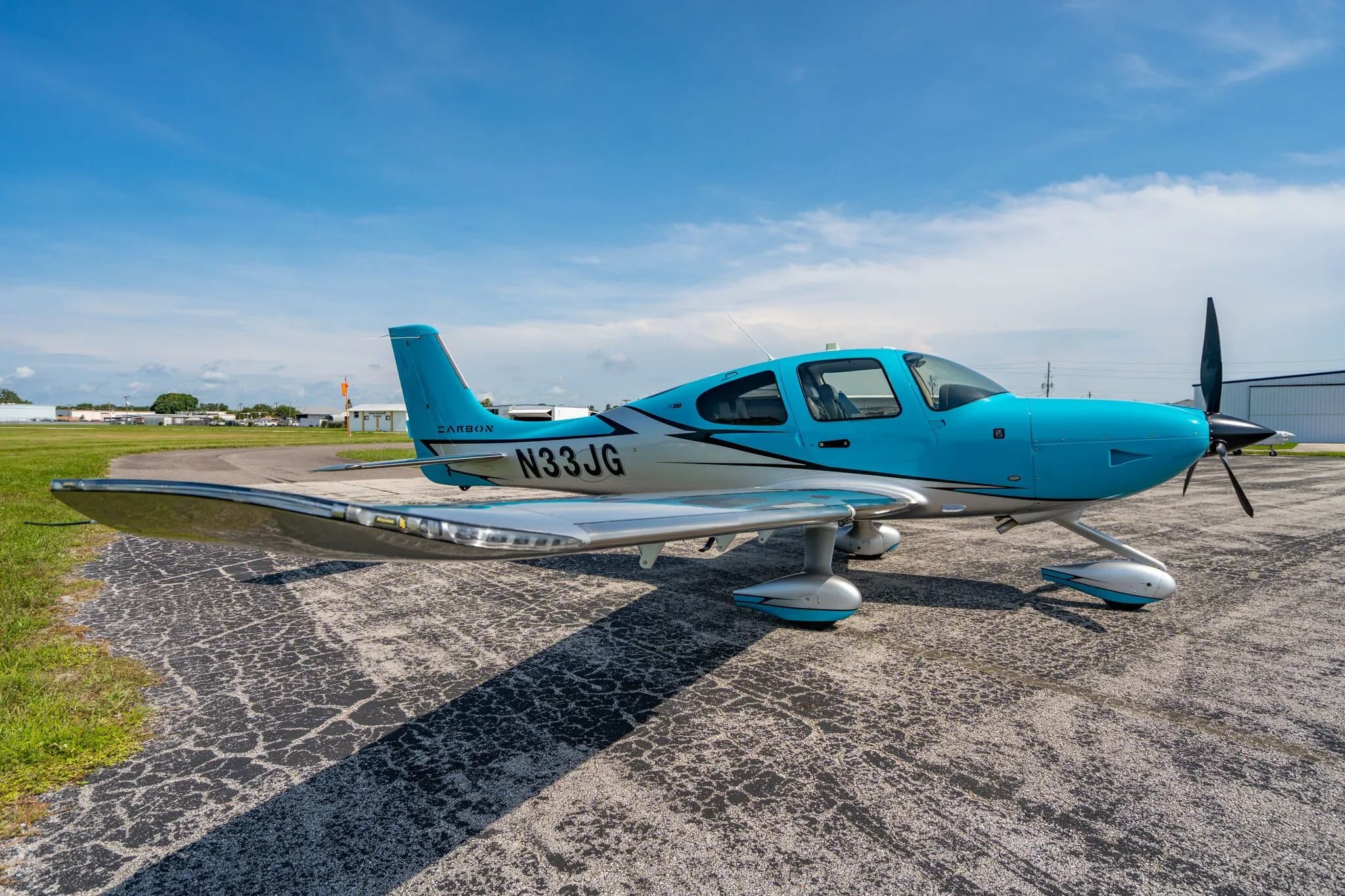 A three-quarter front view of a blue and silver Carbon aircraft (N33JG) parked on an asphalt ramp.