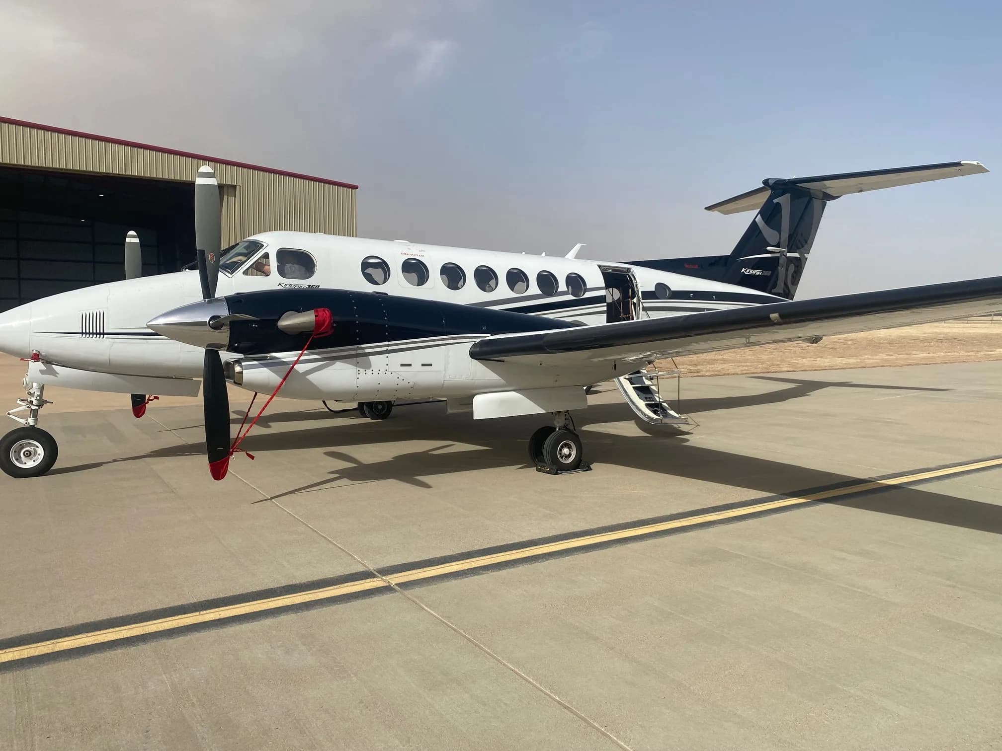 A white twin-engine turboprop aircraft with black and red stripes parked on a tarmac.