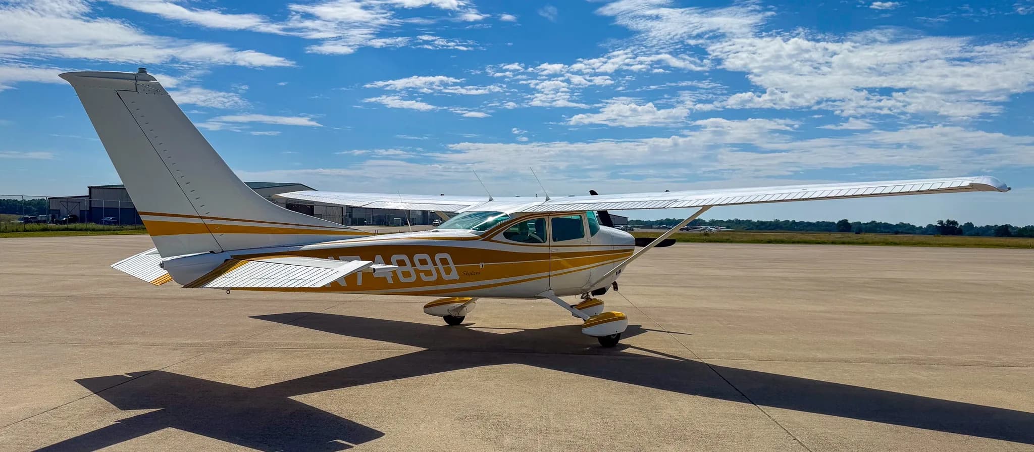 A white and gold Cessna Skylane N7489Q is parked on an airfield tarmac, viewed from the left-rear side.