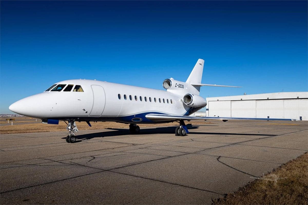 A white and blue Dassault Falcon 900EX, registration C-GEOS, parked on the tarmac.