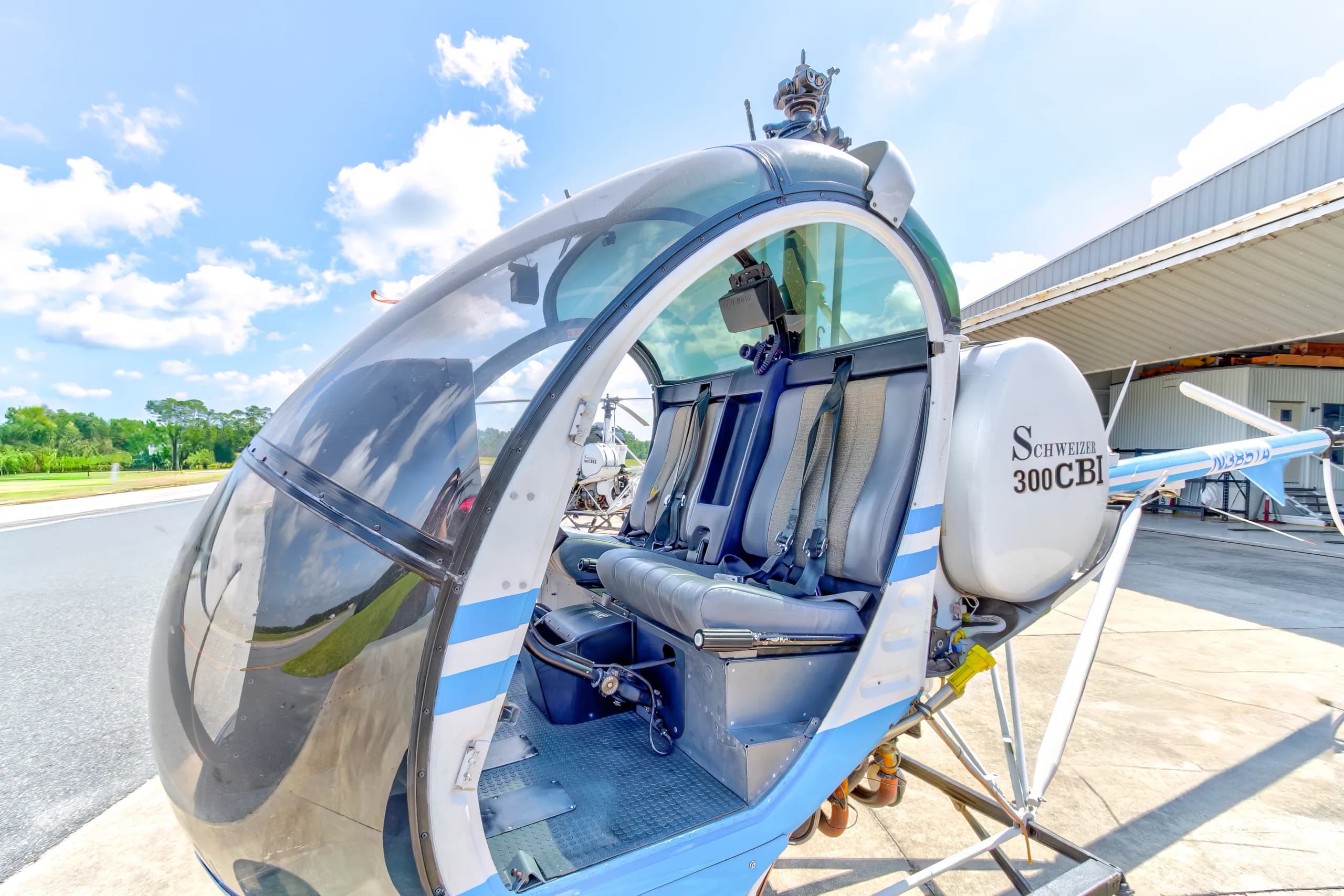 The interior cabin of a blue and white Schweizer 300CBi helicopter, N385TA, showing the seats and part of the exterior fuselage.