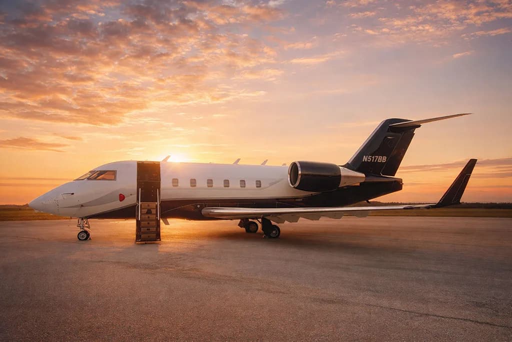 A white and dark blue private jet with registration N517BB has its door open with stairs on an airfield at sunset.