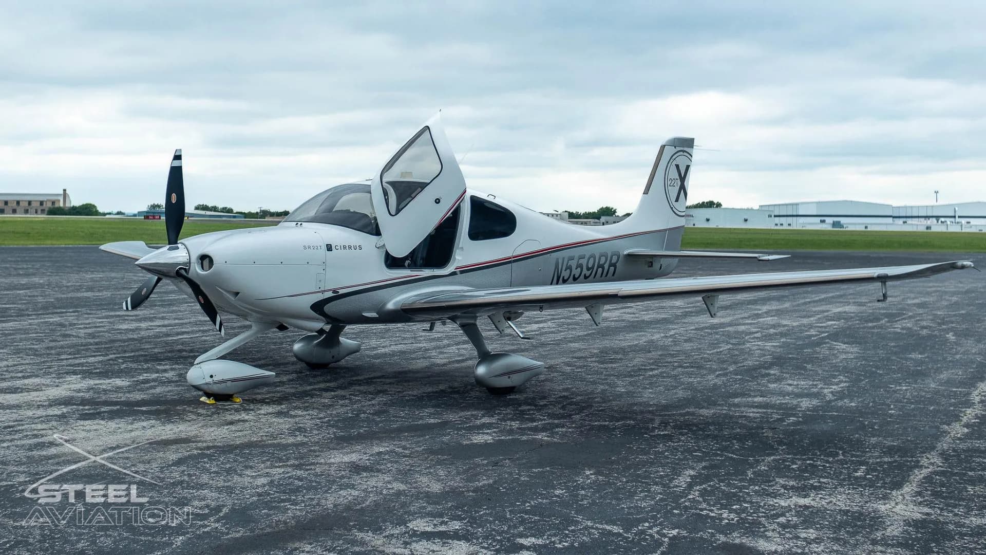A white and silver Cirrus SR22T aircraft with registration N559RR has its gull-wing doors open on an airfield.