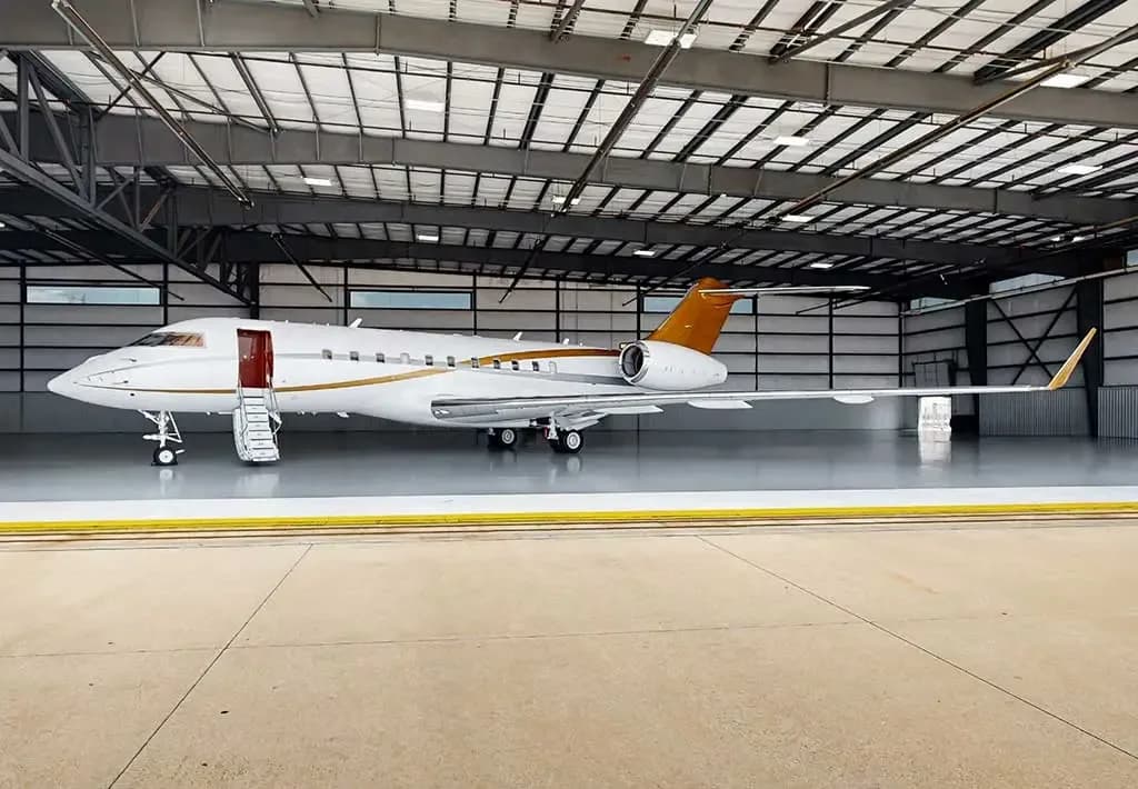 A white business jet with gold accents and an open door with stairs is parked inside a hangar.