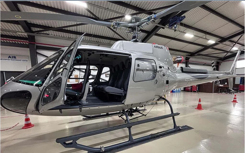 A silver Airbus H125 helicopter with its doors open, parked inside a hangar.