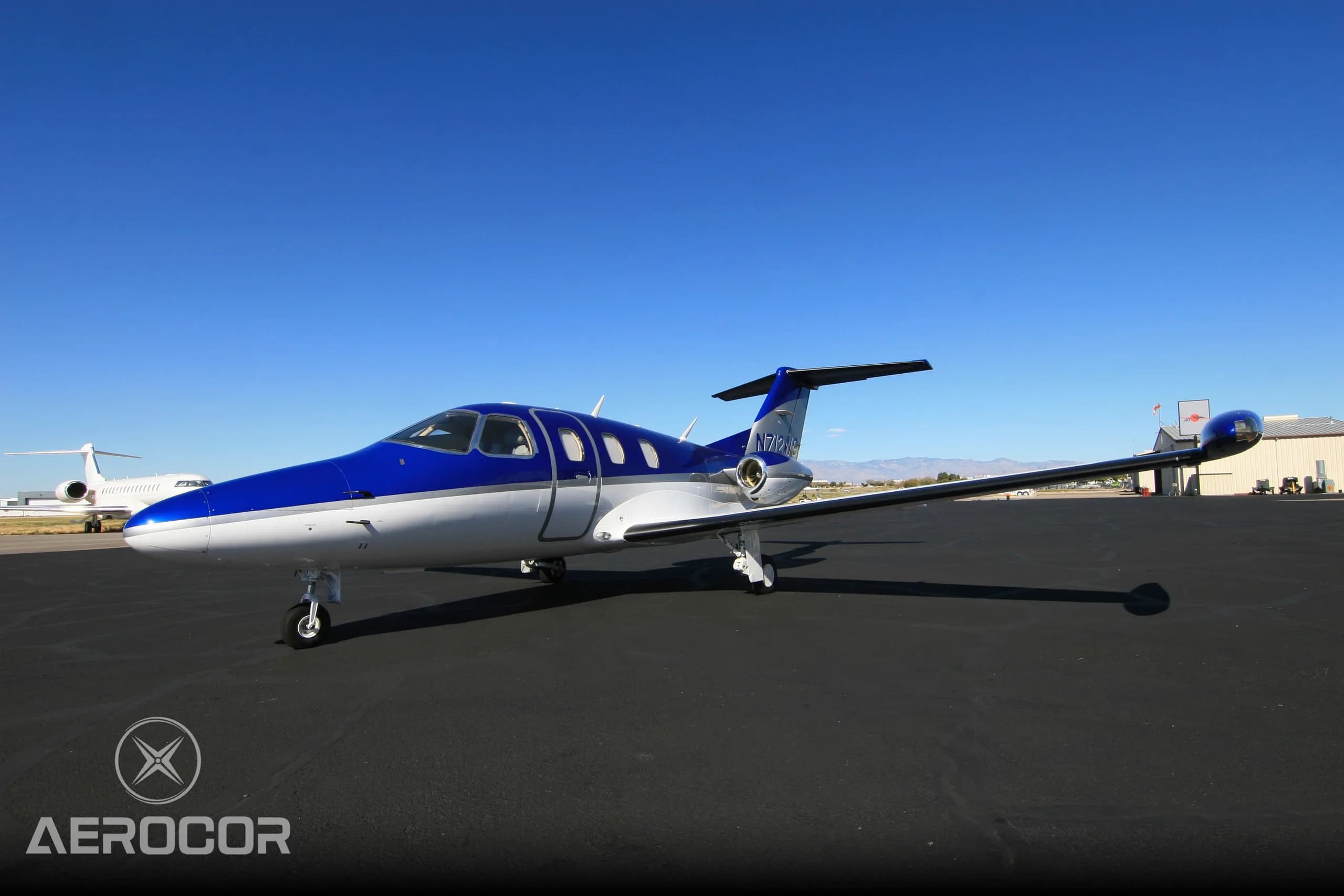 A blue and white Eclipse 500/550 jet, N712WG, parked on an airport tarmac under a clear blue sky.