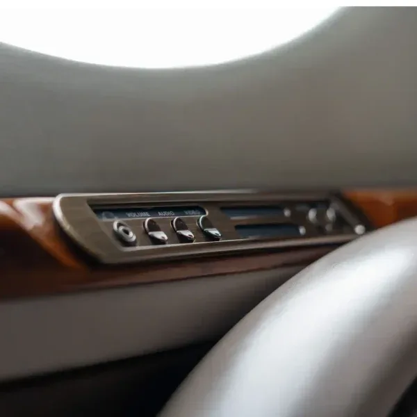 A close-up of an in-cabin entertainment control panel with volume, audio, and video buttons set into a wood-paneled wall.