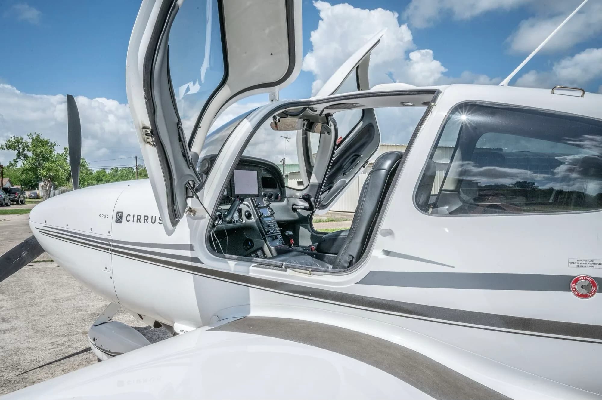 A close-up side view of the white Cirrus SR22 GTS aircraft with both doors open, revealing the cockpit and interior.