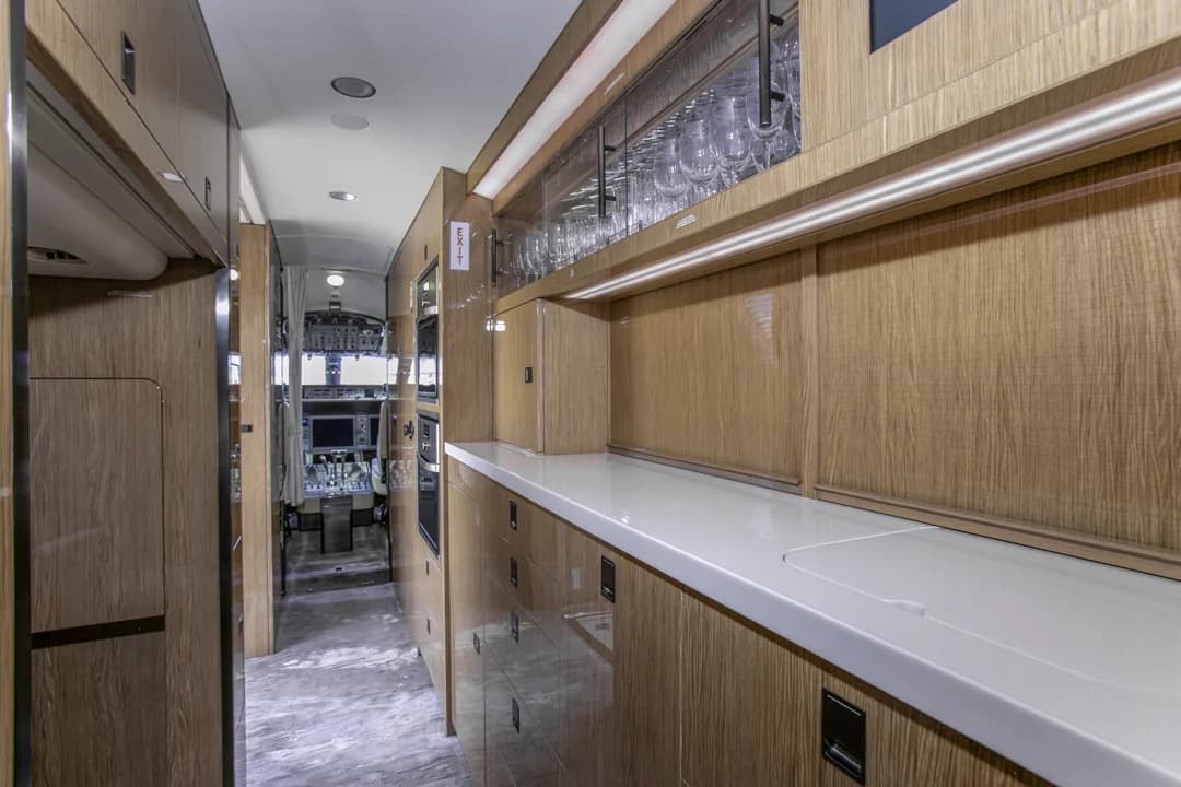 A luxurious aircraft galley with extensive wooden cabinetry, white countertops, and glassware storage.