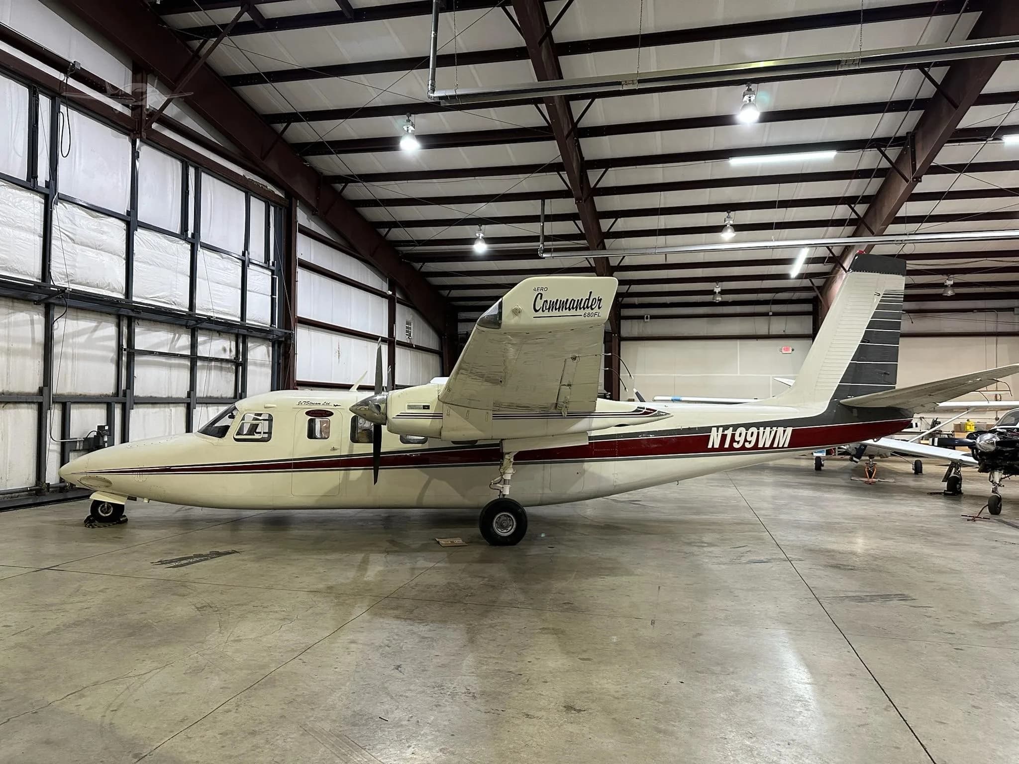 A white and maroon Commander 690A twin-engine aircraft, tail number N199WM, parked in a hangar.