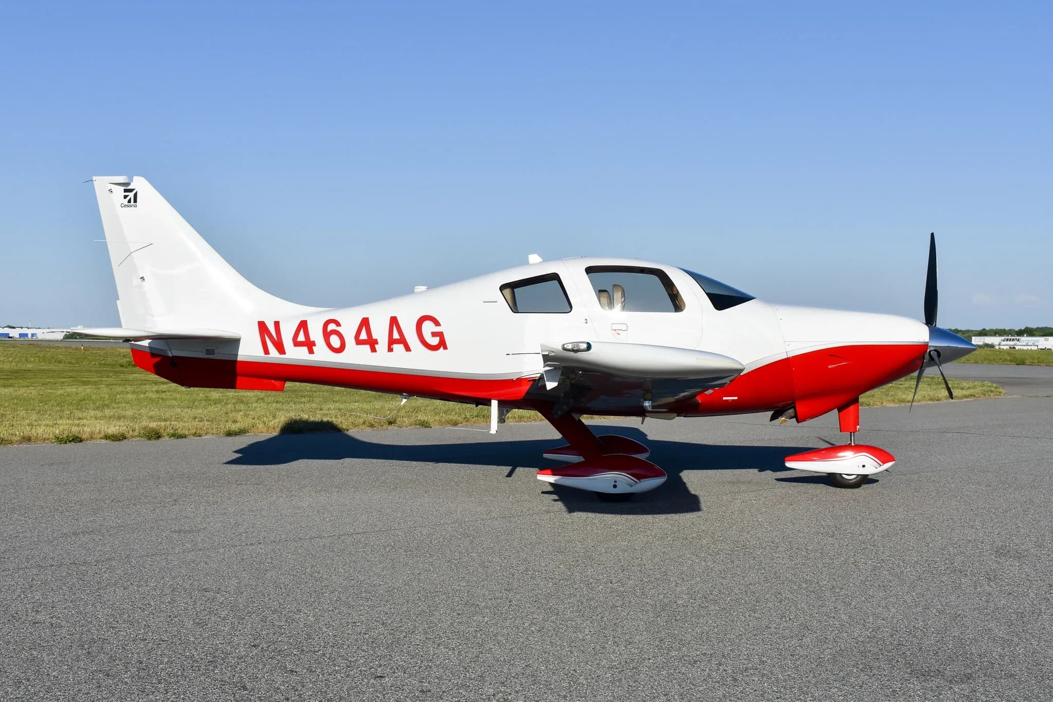 A white and red Cirrus SR22 aircraft, registration N464AG, parked on an airfield under a clear blue sky.