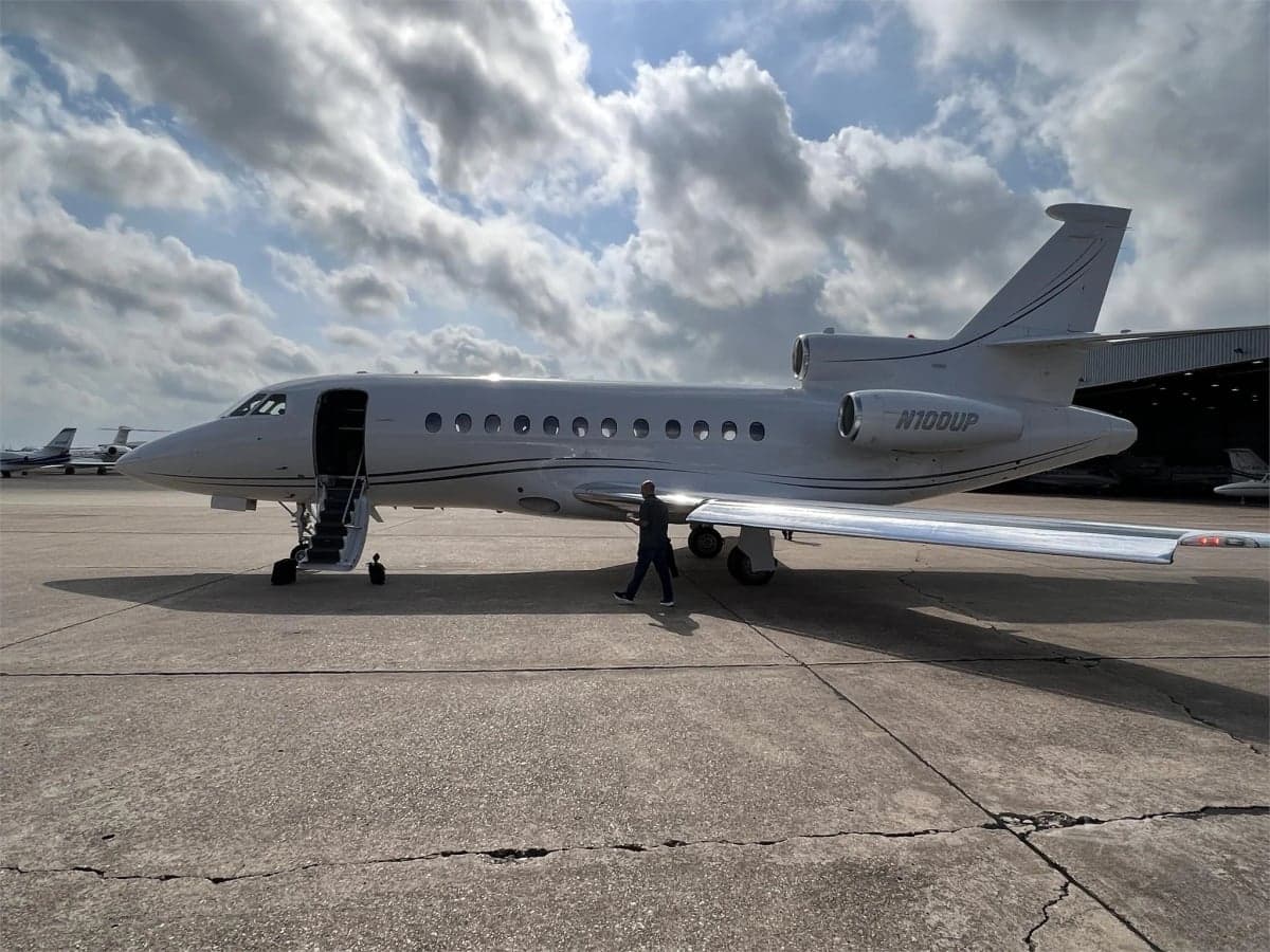 A white Falcon jet, registration N100UP, parked on the tarmac.