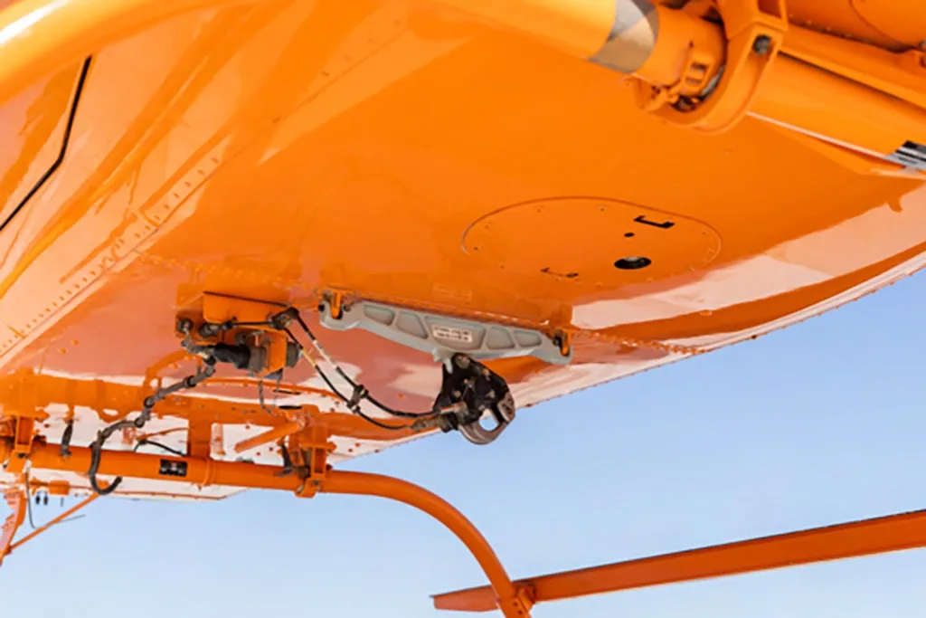A close-up view of the orange underside of the helicopter, showing a cargo hook system.