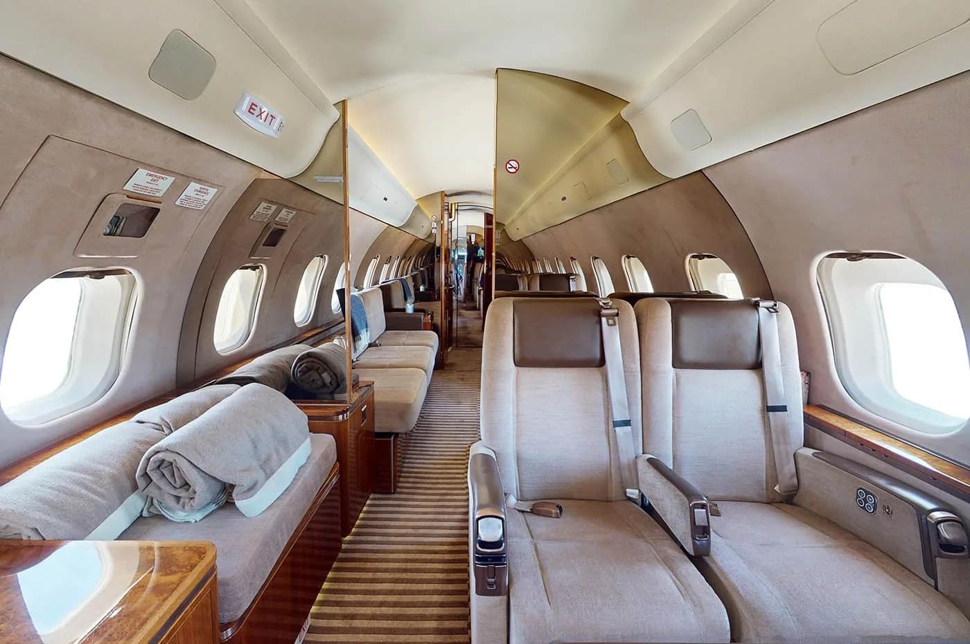 A view inside a private jet cabin, showing beige seats on the right and a lounge sofa with blankets on the left.
