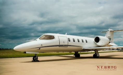 A white business jet with a black stripe is parked on a tarmac under a cloudy sky.