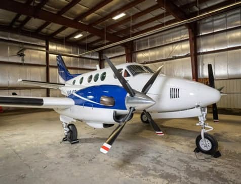 A white and blue Beechcraft King Air aircraft is parked inside a hangar.
