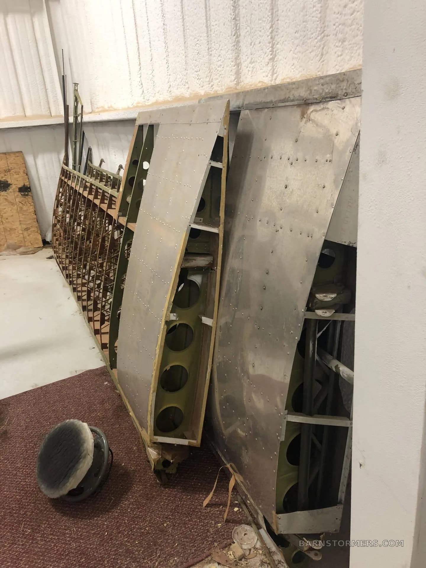 Several disassembled aircraft wing sections, some with exposed internal structure, leaning against a wall in a hangar.