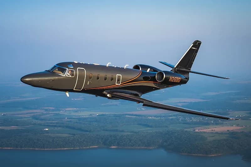 A dark gray jet with orange stripes, registration N26BD, in flight over a rural landscape.